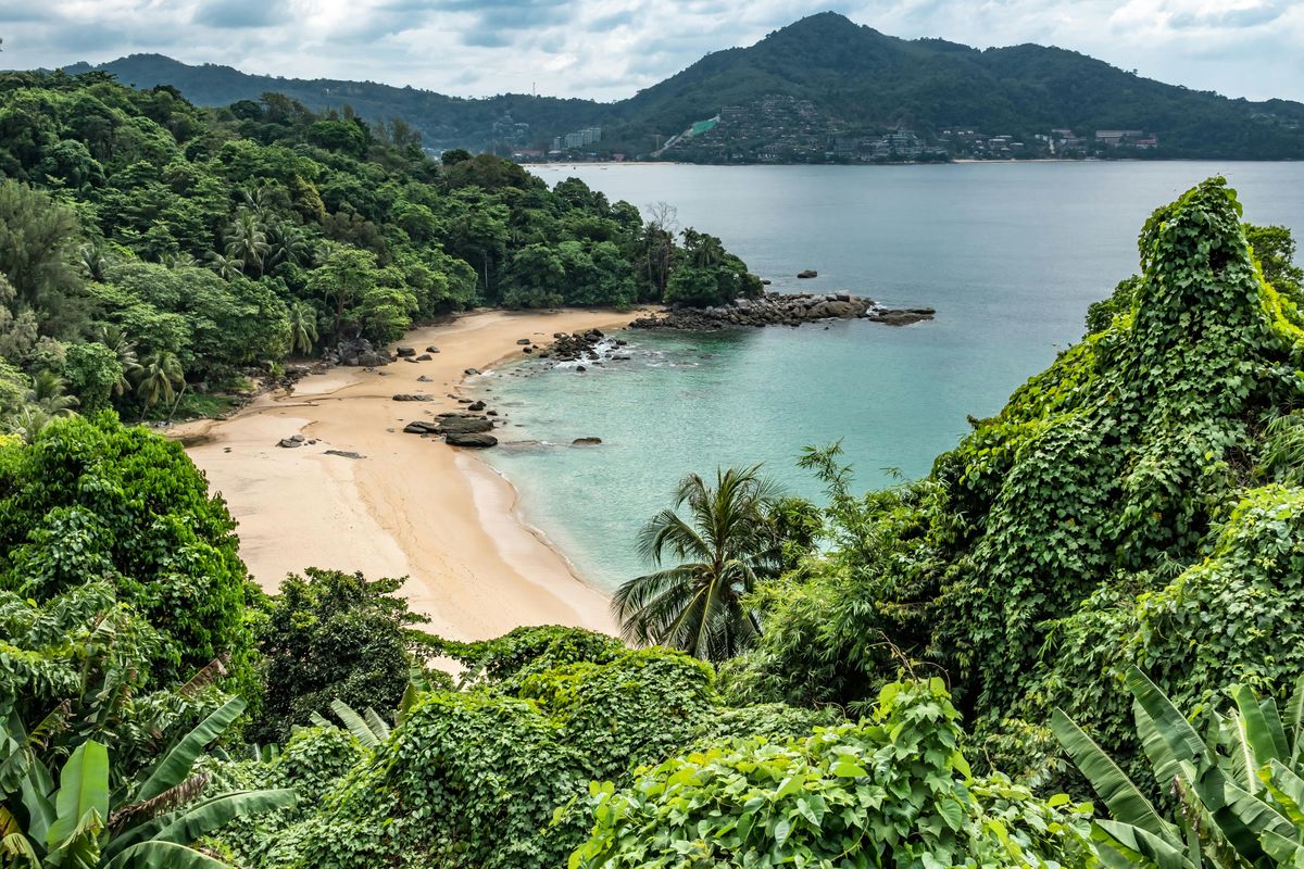 Aerial view of a secluded sandy bay with turquoise water surrounded by lush tropical jungle hills in Phuket, Thailand